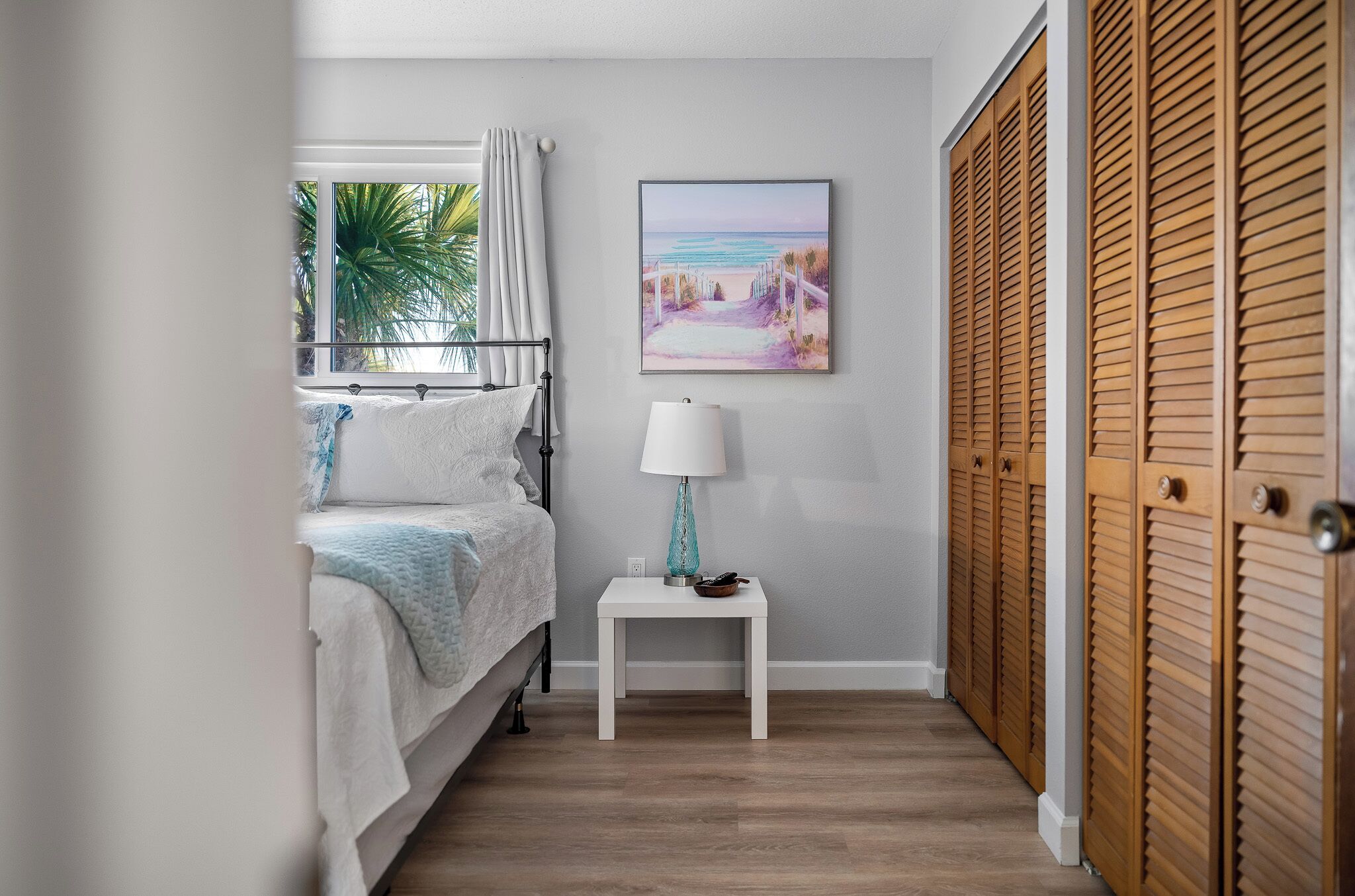 A bedroom with a bed, a bedside table with a lamp, a window with curtains, and a wooden closet.