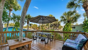 A wooden deck with a picnic table and umbrella, surrounded by palm trees and a view of a pool. - 50 steps to uncrowded beach - 2 king beds - Pac Man arcade - summer beach fun! (Englewood)