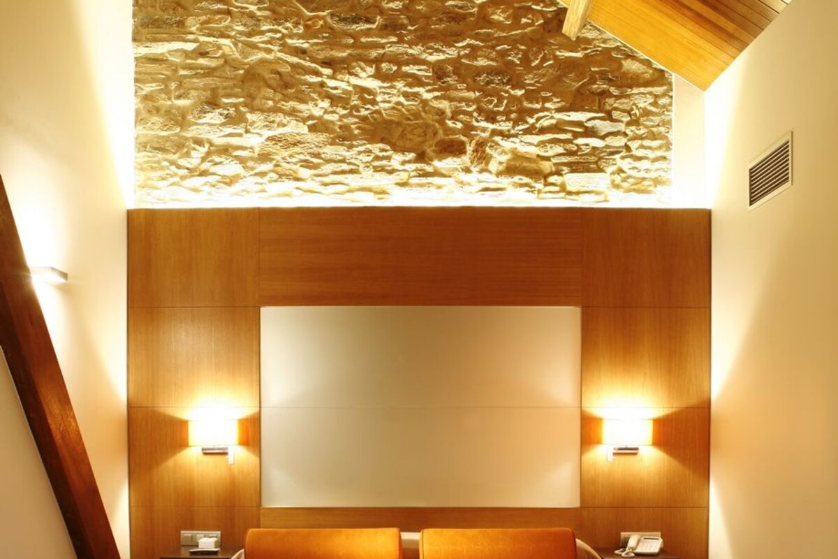 A hotel room with a large bed, wooden headboard, two bedside tables with lamps, and a bench.