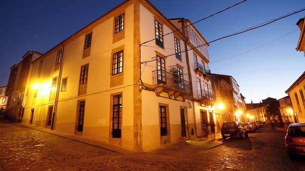 A historic building with multiple windows and a balcony, situated on a cobblestone street.