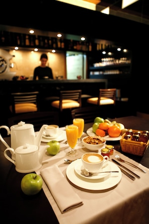 A breakfast table set with a coffee pot, cups, a plate of fruit, and a basket of pastries. - Hotel Altair (Santiago de Compostela)