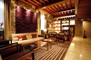 A cozy living area with a stone wall, wooden ceiling, and a seating arrangement including a sofa and chairs. - Hotel Altair (Santiago de Compostela)