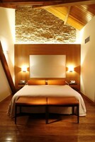 Una habitación de hotel con una cama grande, cabecera de madera, dos mesitas de noche con lámparas y un banco.