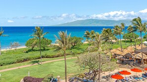 Ein tropisches Resort mit Blick auf den Strand, Liegestühlen und einer Struktur mit Reetdach.