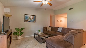 A living room with a brown sofa, a coffee table, a potted plant, and a ceiling fan.