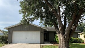 A single-story house with a garage, a driveway, and a large tree in front.