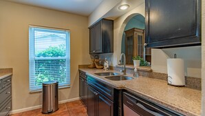 A kitchen with dark cabinets, granite countertops, a stainless steel sink, and a trash can.