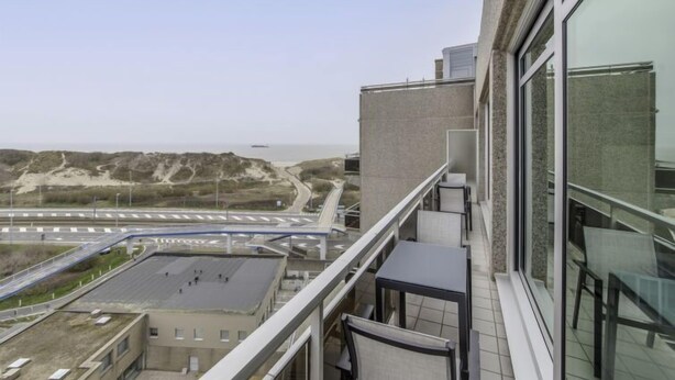 A high-rise building with a balcony overlooking a coastal landscape, including a road and distant ship. - Seaview 4 with parking by Interhome (Bredene)