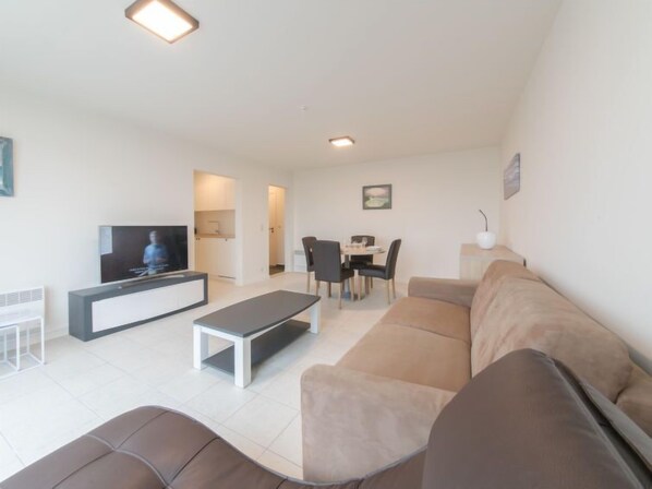 A modern living room with a sofa, a coffee table, a TV, and a dining area with chairs and a table. - Seaview 4 with parking by Interhome (Bredene)