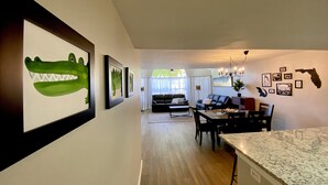 A spacious living room with a dining area, featuring a large green crocodile painting, a chandelier, and a Florida state map on the wall. - Fully Remodeled  stylish 3/2 condo, close to the parks (kissimmee)