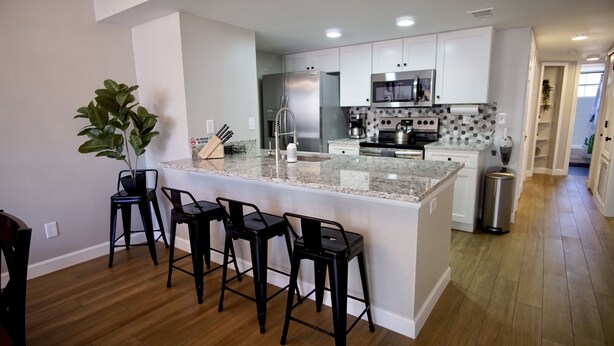 A modern kitchen with a granite island, stainless steel appliances, and black bar stools. - Fully Remodeled  stylish 3/2 condo, close to the parks (kissimmee)