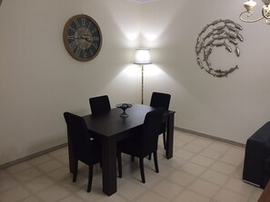 A dining area with a round table and chairs, a wall clock, a floor lamp, and decorative wall art.