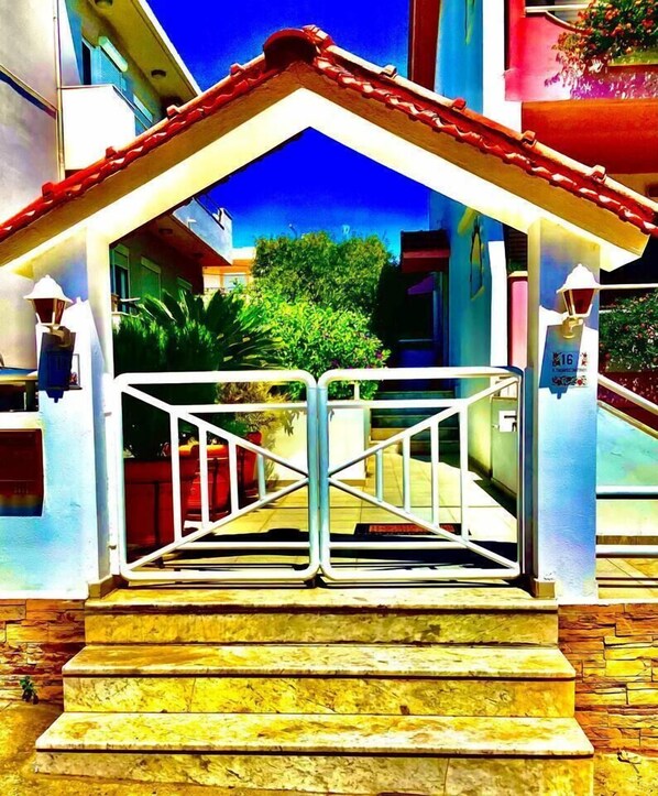 A gated entrance with a metal gate, steps leading up to a porch, and a building in the background.