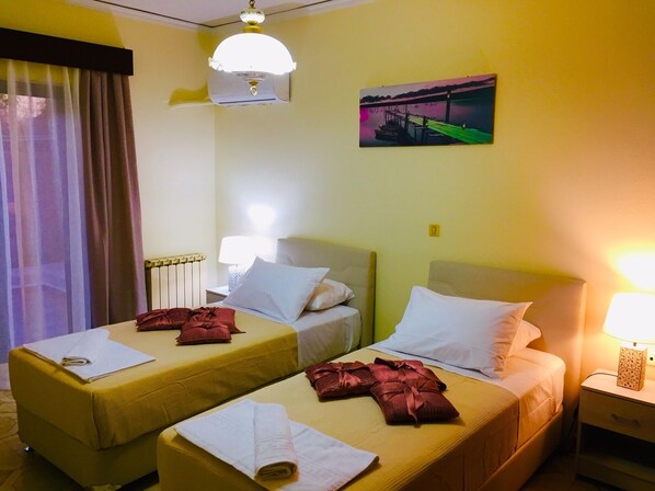 A hotel room with two single beds, a painting of a bridge, a ceiling fan, and a nightstand with a lamp.
