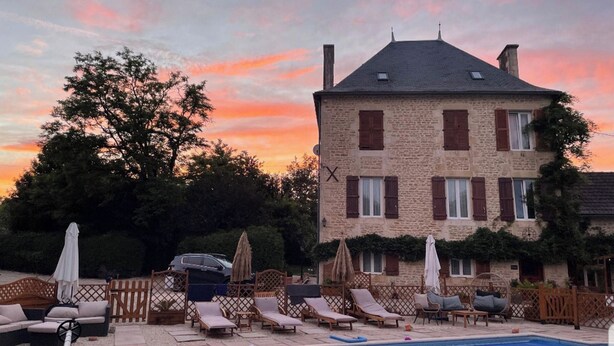 Un edificio de piedra con piscina, sillas de descanso y sombrillas.