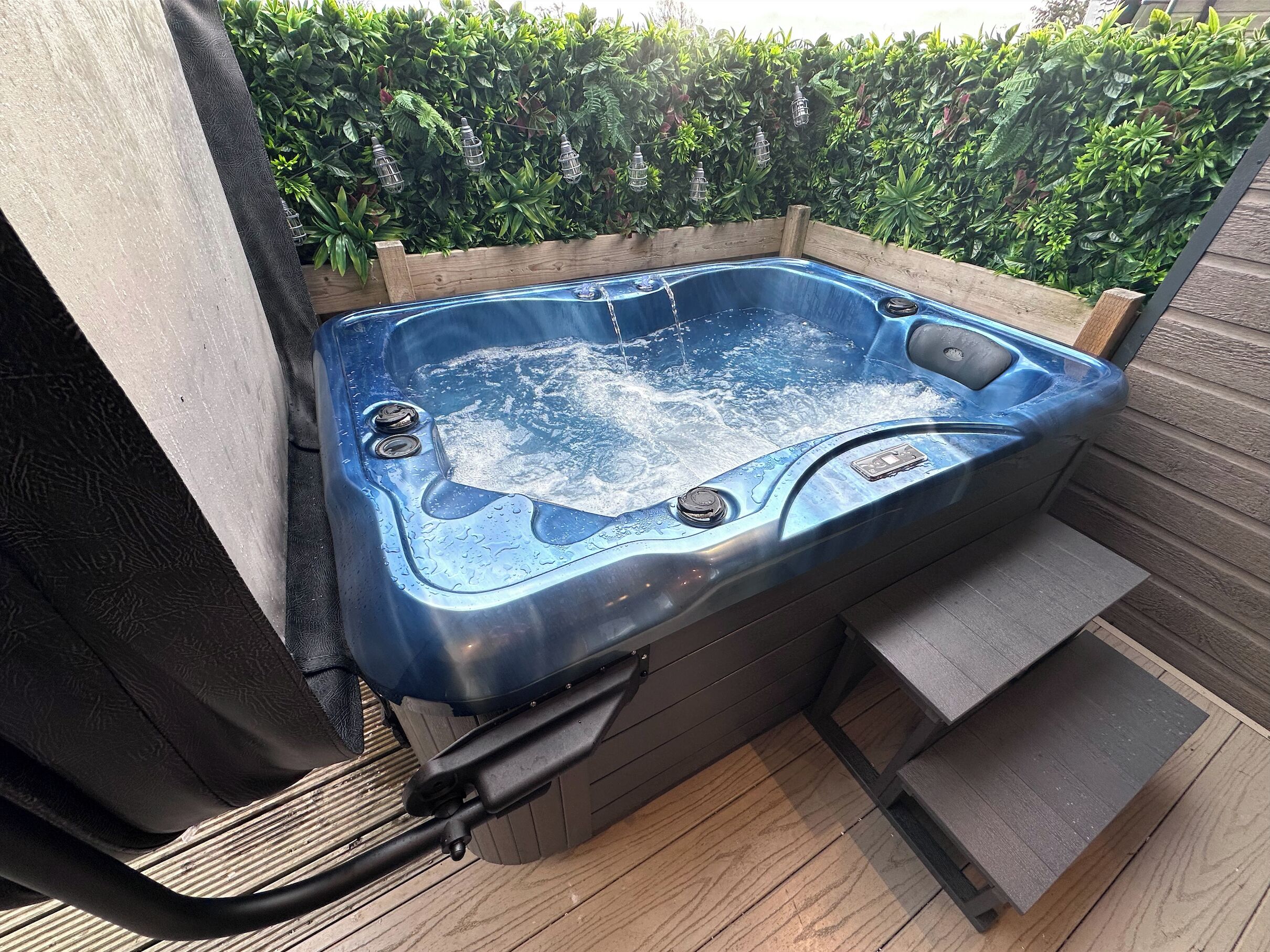 Un jacuzzi con cubierta de madera y una valla de madera al fondo.