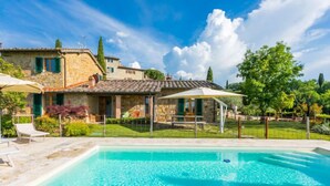 Ein Swimmingpool mit einer Steindeck, einer überdachten Terrasse und einem Haus mit einem Ziegeldach.