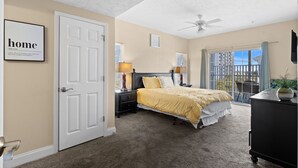 A bedroom with a bed, nightstands, a ceiling fan, a door, and a window with a view. - Full house (Myrtle Beach)