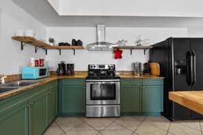 Une cuisine avec des armoires de couleur turquoise, une cuisinière en acier inoxydable, un réfrigérateur noir et des étagères en bois au-dessus du plan de travail.