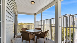 A covered patio with a round table and wicker chairs, overlooking a residential area. - Full house (Myrtle Beach)