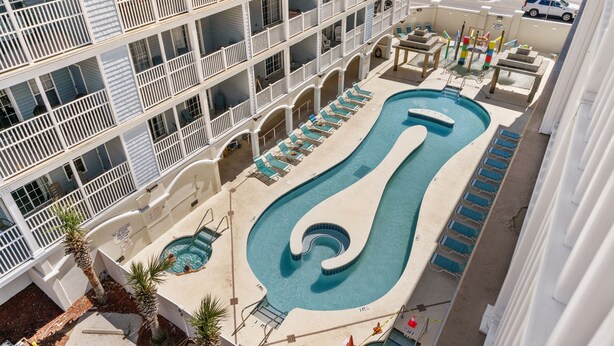 A multi-story hotel with a pool area featuring a unique spiral design, multiple lounge chairs, and a view of the surrounding street. - Full house (Myrtle Beach)