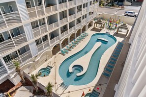 Un hotel de varios pisos con una zona de piscina que presenta un diseño espiral único, múltiples sillones de descanso y vistas de la calle circundante.