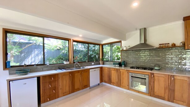 A modern kitchen with wooden cabinets, a built-in oven, and a large window overlooking a garden.