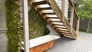 A wooden staircase leading to a white bathtub on a wooden deck.