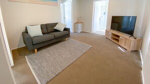 A living room with a sofa, a TV, a painting, and a door leading to a bathroom.