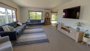 A living room with a sectional sofa, a TV mounted on the wall, and a large window.
