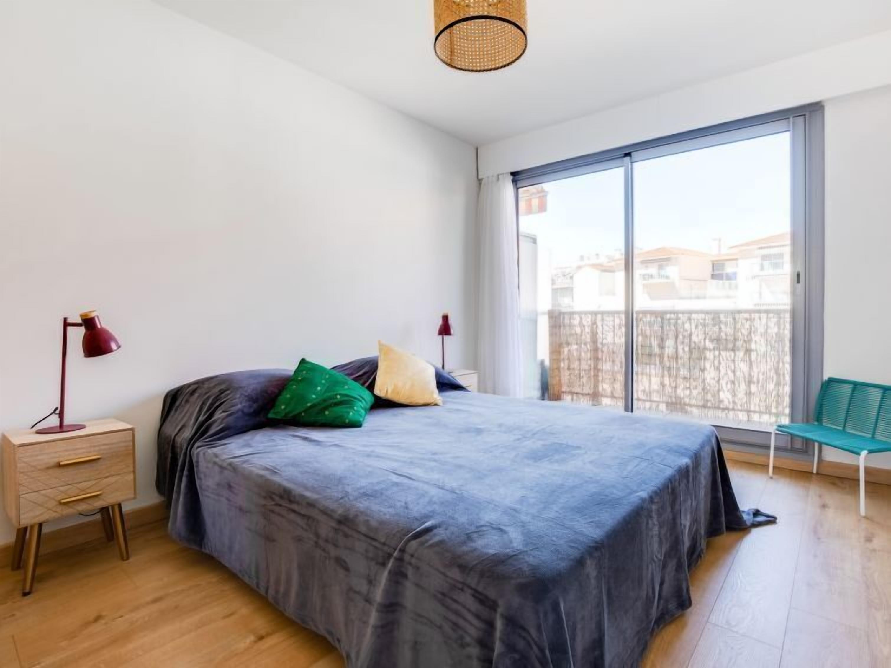 Un dormitorio con una cama grande, una mesita de noche, una lámpara y vistas al exterior a través de una puerta corrediza.