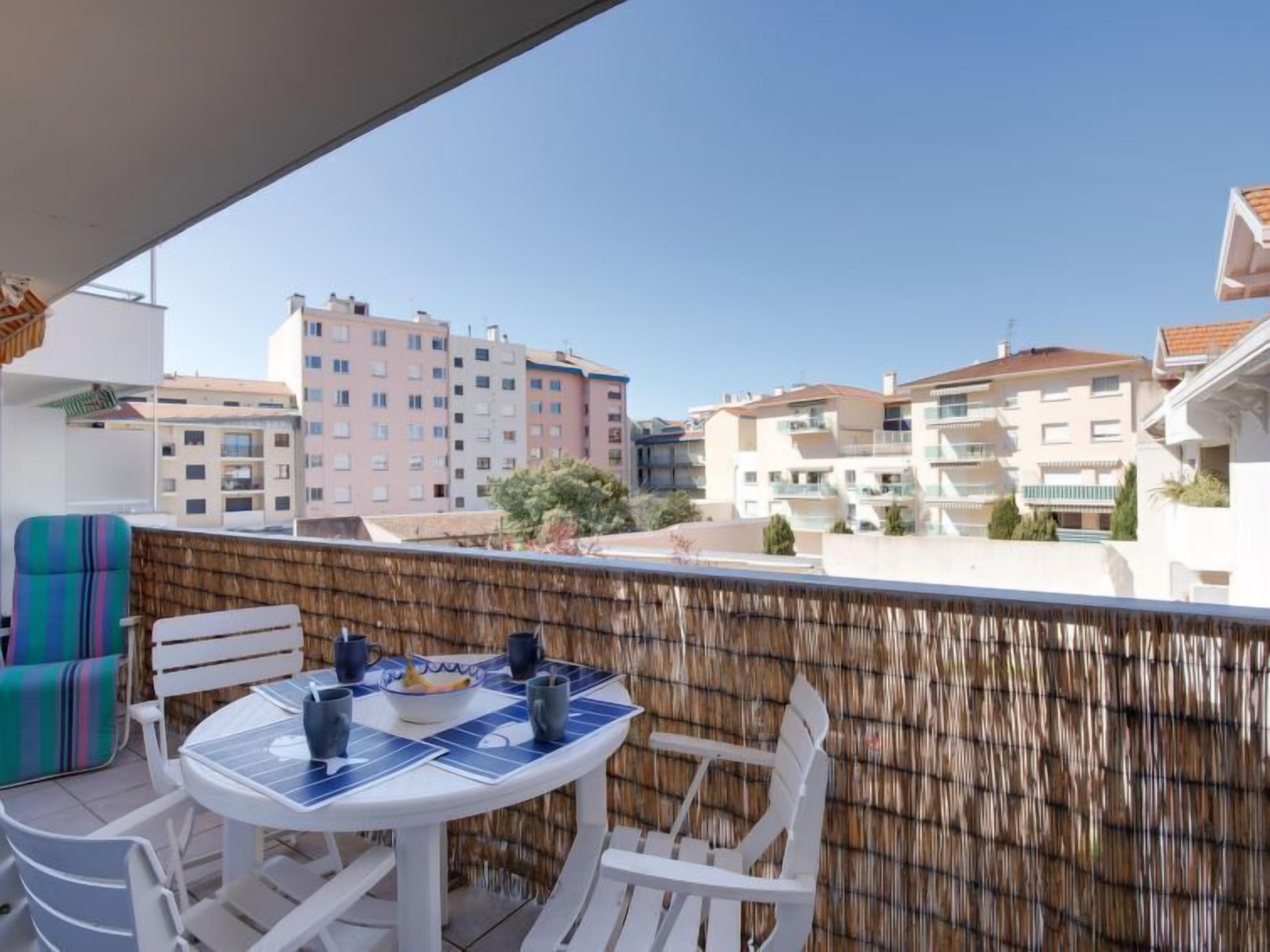 A balcony with a round table and chairs, a woven wall, and a view of multi-story buildings.