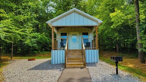 A small, single-story cabin with a porch and a front door, surrounded by trees. - Pet Friendly Tiny House - Lake Guntersville (Guntersville)