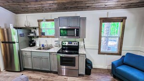 A modern kitchen with stainless steel appliances, wooden ceiling, and large windows. - Pet Friendly Tiny House - Lake Guntersville (Guntersville)
