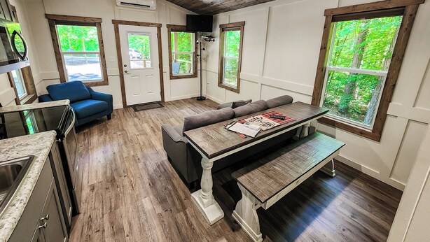 A modern kitchen with wooden flooring, a built-in bench, and a dining table. - Pet Friendly Tiny House - Lake Guntersville (Guntersville)