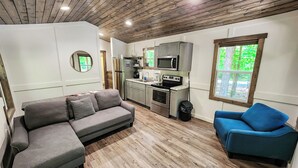 A compact living space with a kitchenette, a grey sectional sofa, a blue armchair, and a wooden ceiling. - Pet Friendly Tiny House - Lake Guntersville (Guntersville)