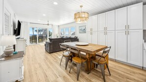 A modern kitchen with white cabinets, a wooden dining table, and a large window overlooking a scenic view. - Amelia Island - Amelia by the Sea 2BR Private Fishing Pier (Fernandina Beach)