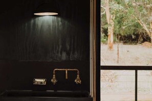 A black interior wall with a window, a brass faucet, and a small rectangular object on the counter. - Carnaby Wandagar Eco Tent—Nature-Immersed Glamping (Pemberton)