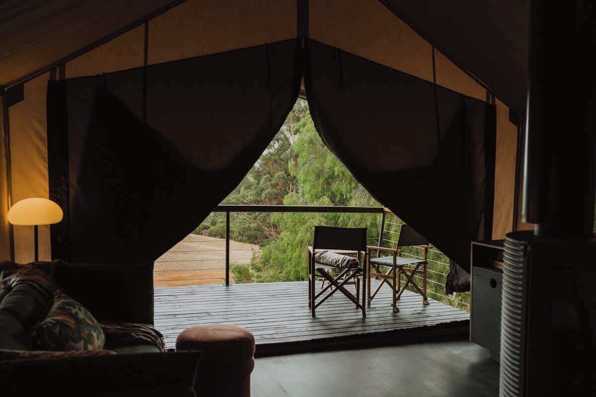 Una carpa con vista a follaje, una mesa con sillas y una lámpara.