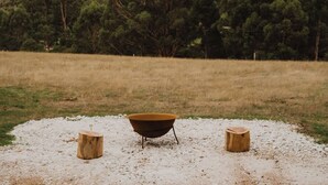 A rustic outdoor setting with a metal basin on a gravel surface, flanked by two wooden stumps.