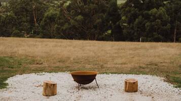 A rustic outdoor setting with a metal basin on a gravel surface, flanked by two wooden stumps.