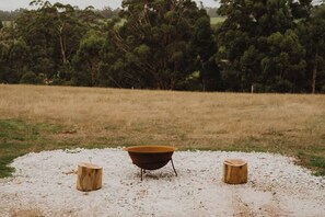 A rustic outdoor setting with a metal basin on a gravel surface, flanked by two wooden stumps.