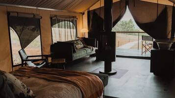 A tented accommodation with a bed, seating area, and a view of the outdoors.