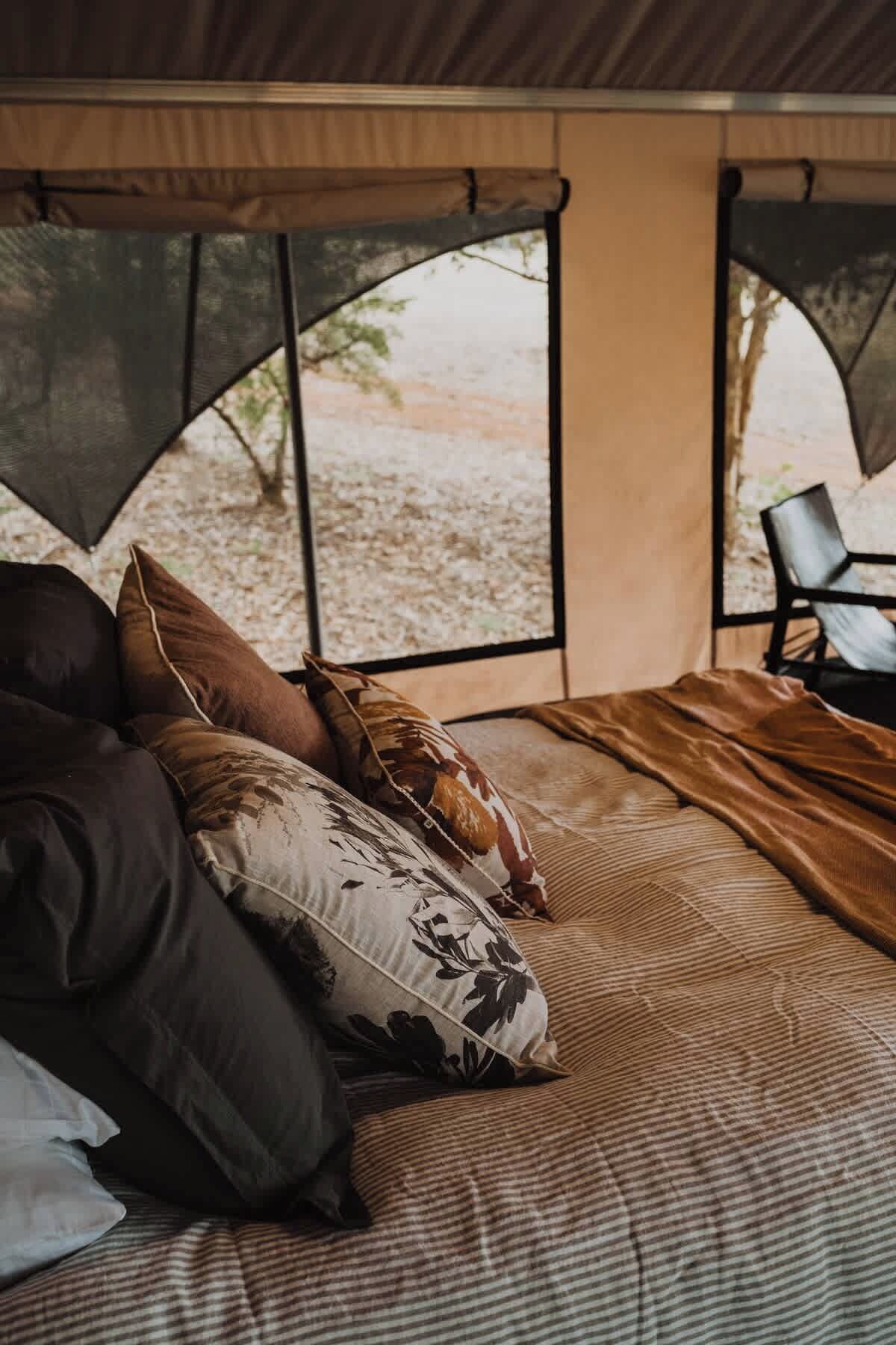 A tent with a bed, pillows, and a chair.