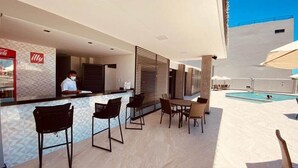 Un espace aménagé au bord de la piscine, avec un bar, des sièges et une vue sur la piscine.