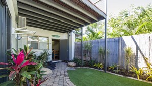 A covered patio area with a stone pathway leading to a door, surrounded by lush greenery and a bamboo fence. - Beachside Cottage - A Private Peaceful Hidden Gem (Nelly Bay)