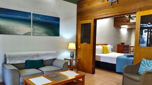 A cozy room with a sofa, a wooden coffee table, and a bed with a nightstand. - Beachside Cottage - A Private Peaceful Hidden Gem (Nelly Bay)