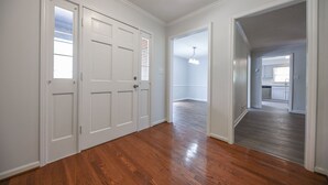 Un couloir avec un plancher en bois, des portes blanches et une cuisine visible au fond.