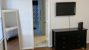 Une chambre à coucher comprenant un lit, une commode, un téléviseur et une porte donnant sur une autre pièce.