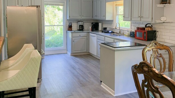 Une cuisine moderne avec des meubles de couleur gris clair, un grand îlot central et un coin repas agrémenté d’une chaise en bois.